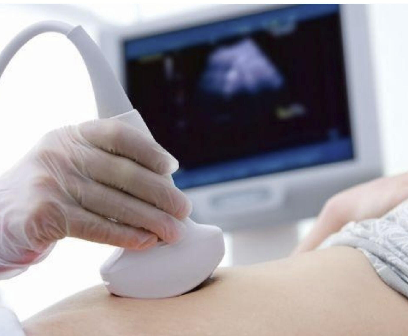 A picture of a hand holding an ultrasound probe, scanning an abdomen and an ultrasound screen in the background